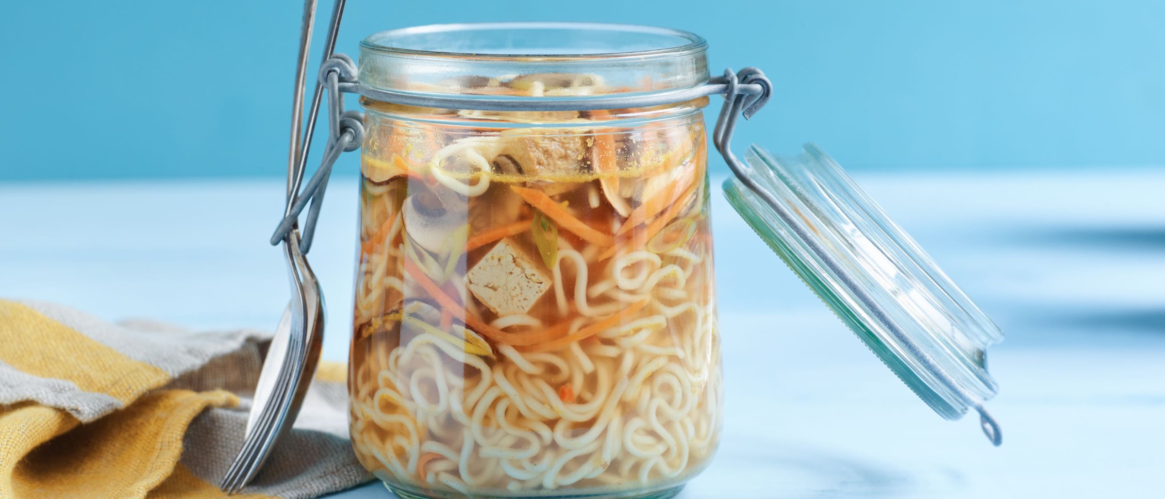 Alnatura Rezept: Ein Glas mit Instant Nudelsuppe mit einem Esslöffel auf einem Tisch.