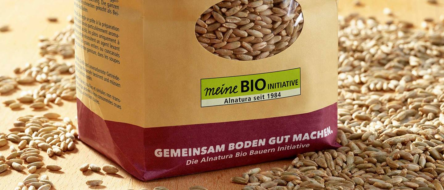 Getreidekörner liegen lose auf dem Tisch und dazwischen steht eine Packung mit Getreidekörnern von Alnatura